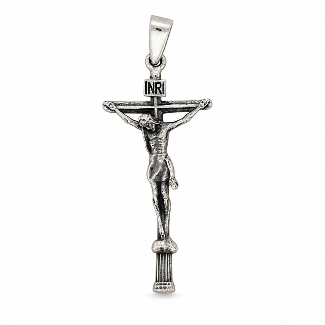 Dije de cruz con Cristo en plata ley 925 con placa INRI y base estriada sobre fondo blanco.